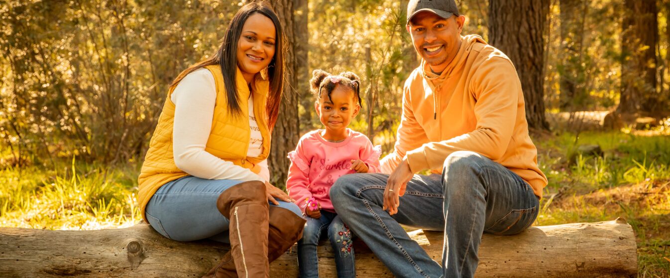 Family sitting on log in forest.
